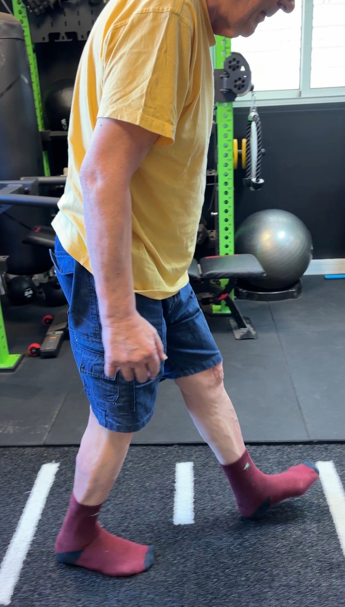 Personne accompagnée, cadrée sous le menton, en position de pas avant sur un tapis d'entraînement. Le visage n'est pas visible.